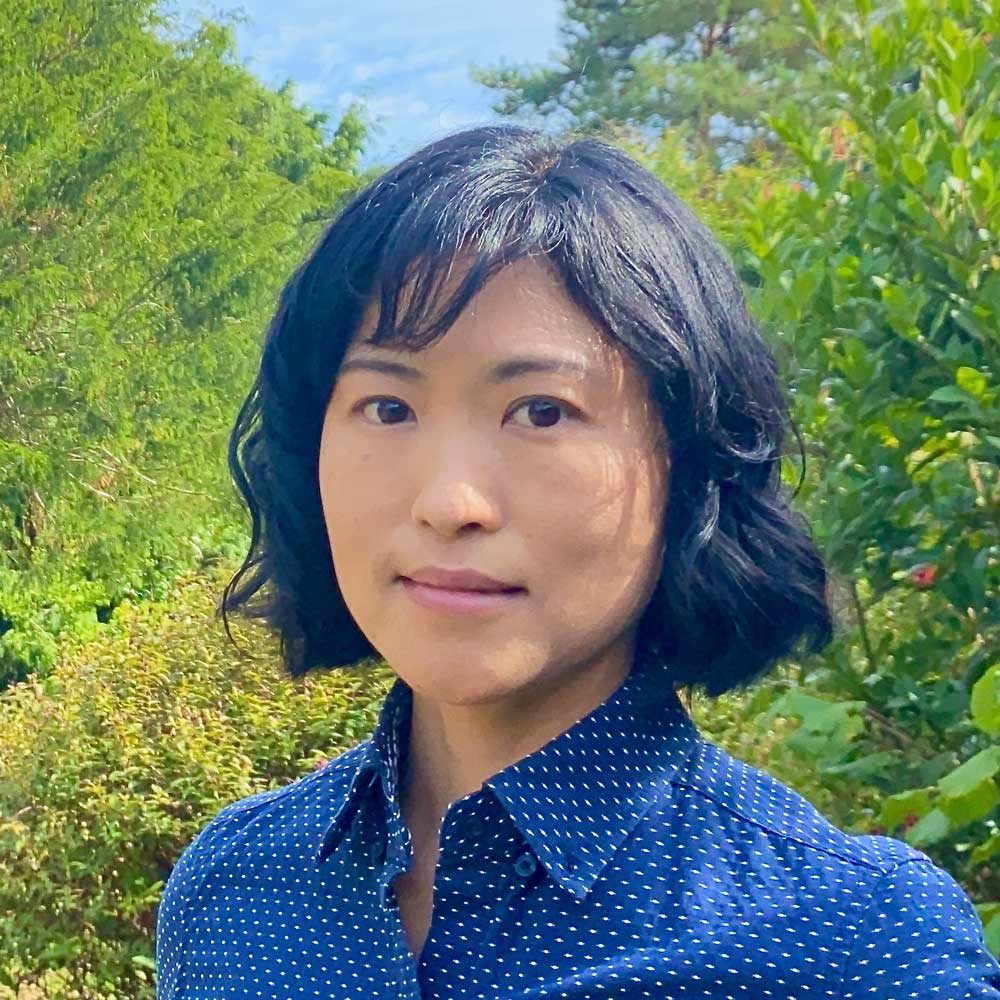 Portrait photo of Maki Tamaki-Briggs smiling at camera in a sunny garden