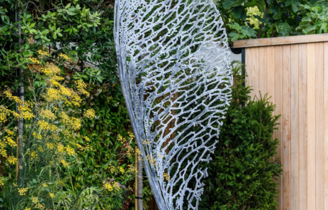 A large metal sculpture of a propeller seed in a stylish garden