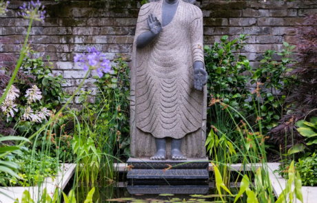 A stone sculpture of Buddha at the head of a stylish water feature in a modern garden,