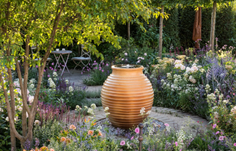 A large terracotta pot water feature surrounded by colourful flowers