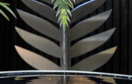 A stylish water feature with a large white bowl and curved metal leaf